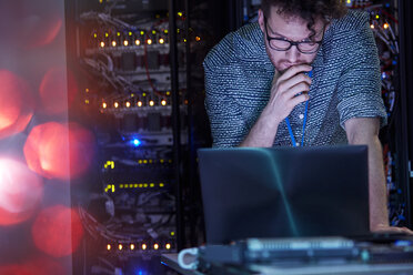 Fokussierter männlicher IT-Techniker, der in einem dunklen Serverraum an einem Laptop arbeitet - CAIF07385