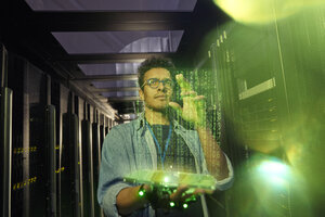 Male IT technician using futuristic digital tablet in dark server room - CAIF07389