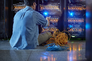 Männlicher IT-Techniker mit Kabeln an einer Tafel in einem dunklen Serverraum - CAIF07396