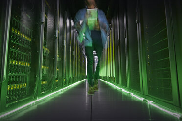 IT-Techniker geht durch einen dunklen, leuchtenden Serverraum - CAIF07400