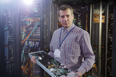 Portrait male IT technician holding panel in server room - CAIF07401