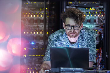 Fokussierter männlicher IT-Techniker, der in einem dunklen Serverraum an einem Laptop arbeitet - CAIF07404