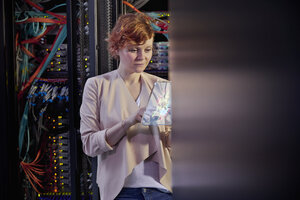 Female IT technician using futuristic digital tablet in server room - CAIF07406