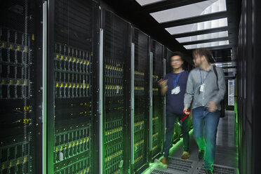 IT technicians walking and talking in dark server room - CAIF07423