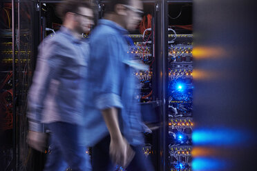 Male IT technicians walking in dark server room - CAIF07426