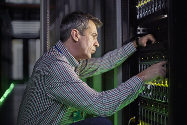 Fokussierter männlicher IT-Techniker bei der Arbeit an einer Schalttafel in einem dunklen Serverraum - CAIF07432