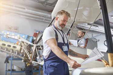 Männlicher Maschinenbauingenieur, der Pläne an einem Flugzeug im Hangar überprüft - CAIF07436