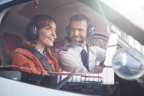 Pilot im Gespräch mit einem lächelnden Passagier im Cockpit eines Flugzeugs - CAIF07437