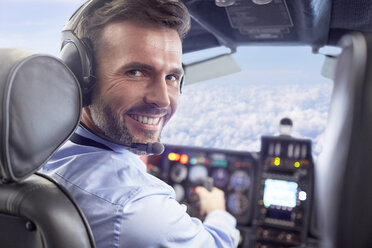 Porträt eines lächelnden, selbstbewussten männlichen Piloten, der ein Flugzeug im Cockpit fliegt - CAIF07448