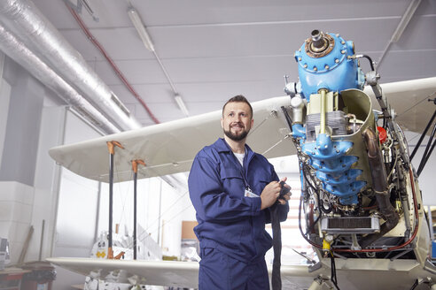 Porträt selbstbewusster männlicher Flugzeugmechaniker bei der Arbeit an einem Doppeldecker in einem Hangar - CAIF07458