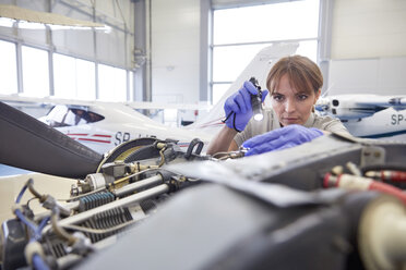 Fokussierter weiblicher Mechaniker mit Taschenlampe, der einen Flugzeugtriebwerk im Hangar untersucht - CAIF07463