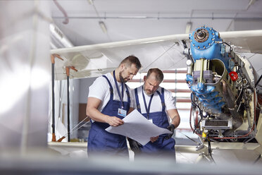 Männlicher Ingenieur-Mechaniker, der Pläne prüft und ein Flugzeug im Hangar repariert - CAIF07464