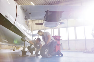 Männliche Mechaniker reparieren Räder an einem Flugzeug im Hangar - CAIF07466