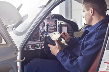 Männlicher Ingenieur, der im Cockpit eines Flugzeugs Diagnosen mit einem digitalen Tablet überprüft - CAIF07470