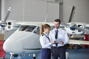 Piloten besprechen Papierkram in der Nähe des Flugzeugs im Hangar - CAIF07472