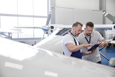 Männlicher Mechaniker, der ein digitales Tablet in der Nähe eines Flugzeugs im Hangar benutzt - CAIF07473