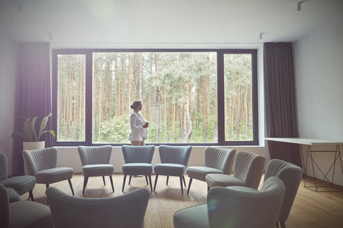 Pensive woman looking out windows at tress in group therapy room - CAIF07480