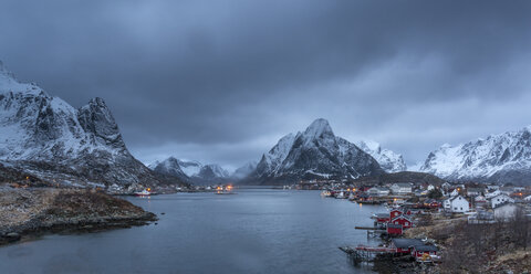 Schneebedeckte Bergkette über dem Fischerdorf in der Abenddämmerung, Reine, Lofoten, Norwegen - CAIF07533