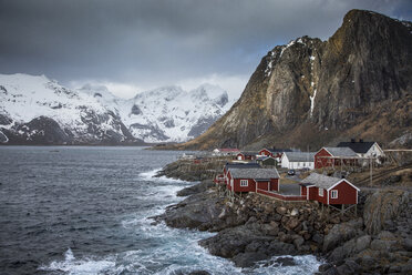 Schneebedeckte Berge hinter einem zerklüfteten Fischerdorf in einer Bucht, Hamnoya, Lofoten, Norwegen - CAIF07544