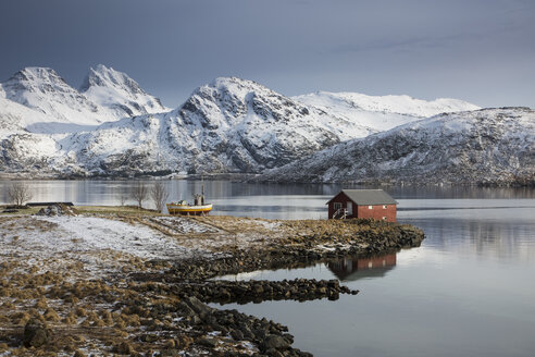 Fischerhütte in einer kalten Bucht unter schneebedeckten Bergen, Norwegen - CAIF07547