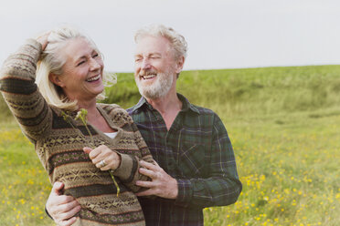 Lächelndes älteres Paar, das sich auf einem Feld umarmt - CAIF07554