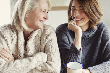 Laughing mother and daughter in sweaters drinking coffee - CAIF07557