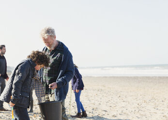 Mehrgenerationen-Familie beim Muschelschürfen am sonnigen Strand - CAIF07566
