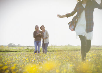 Frauen beobachten Mädchen laufen in sonnigen Wiese mit Wildblumen - CAIF07569