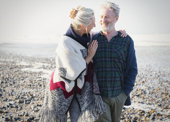 Senior couple hugging and walking on sunny rocky beach - CAIF07571