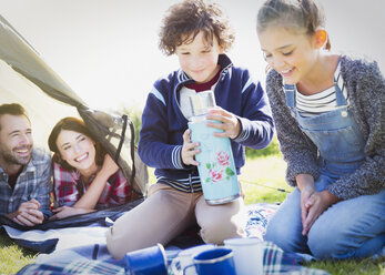 Brother and sister holding insulated drink container outside tent - CAIF07578