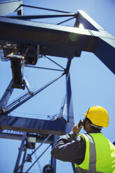 Low angle view of worker using walkie-talkie near crane - CAIF07645