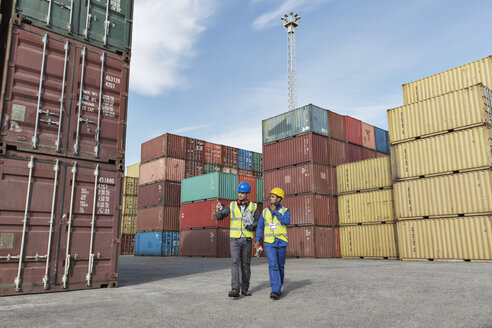 Arbeiter und Geschäftsmann unterhalten sich in der Nähe von Frachtcontainern - CAIF07662