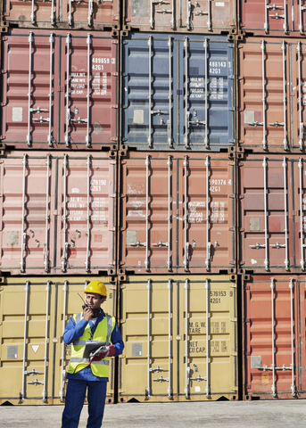 Arbeiter benutzt Walkie-Talkie in der Nähe von Frachtcontainern, lizenzfreies Stockfoto