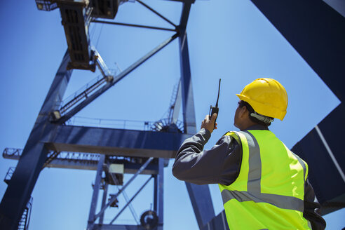 Low angle view of businessman using walkie-talkie under cargo crane - CAIF07665
