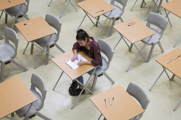 Erhöhte Ansicht einer einzelnen Schülerin, die ihre GCSE-Prüfung im Klassenzimmer schreibt - CAIF07702