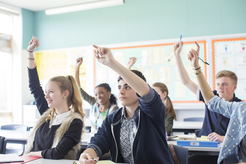 Schüler heben während des Unterrichts im Klassenzimmer die Arme, lizenzfreies Stockfoto