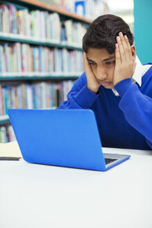 Porträt eines besorgten Studenten, der in der Bibliothek auf seinen Laptop schaut - CAIF07708