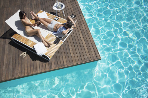 Couple laying on lounge chair at poolside - CAIF07731