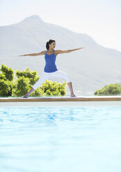 Woman practicing yoga at poolside - CAIF07737