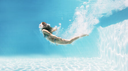 Woman swimming underwater in swimming pool - CAIF07768