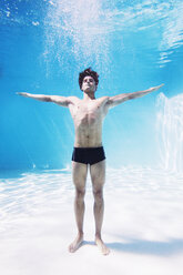 Man standing underwater in swimming pool with arms outstretched - CAIF07772
