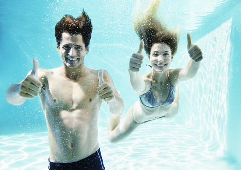 Paar gibt Daumen hoch unter Wasser im Schwimmbad, lizenzfreies Stockfoto