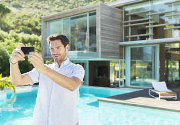 Mann nimmt Selbstporträt mit Fotohandy am Swimmingpool auf - CAIF07845