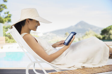 Frau mit digitalem Tablet auf Liegestuhl am Pool - CAIF07846