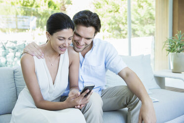 Couple using cell phone on sofa - CAIF07855