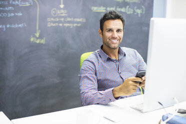 Businessman using cell phone at desk in office - CAIF07880