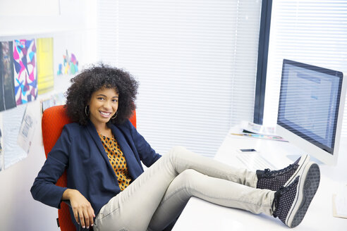 Porträt einer Geschäftsfrau mit hochgelegten Füßen auf dem Schreibtisch - CAIF07917