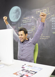 Businessman cheering at desk in office - CAIF07920