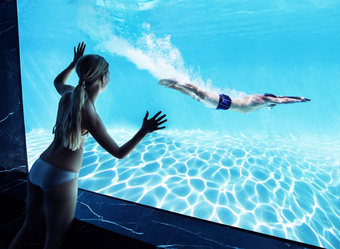 Frau beobachtet ihren Freund unter Wasser im Schwimmbad, lizenzfreies Stockfoto