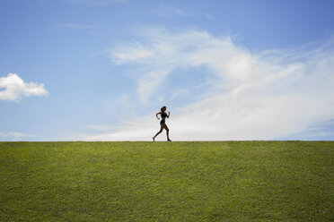 Athlete jogging on grassy field against cloudy sky - CAVF01393